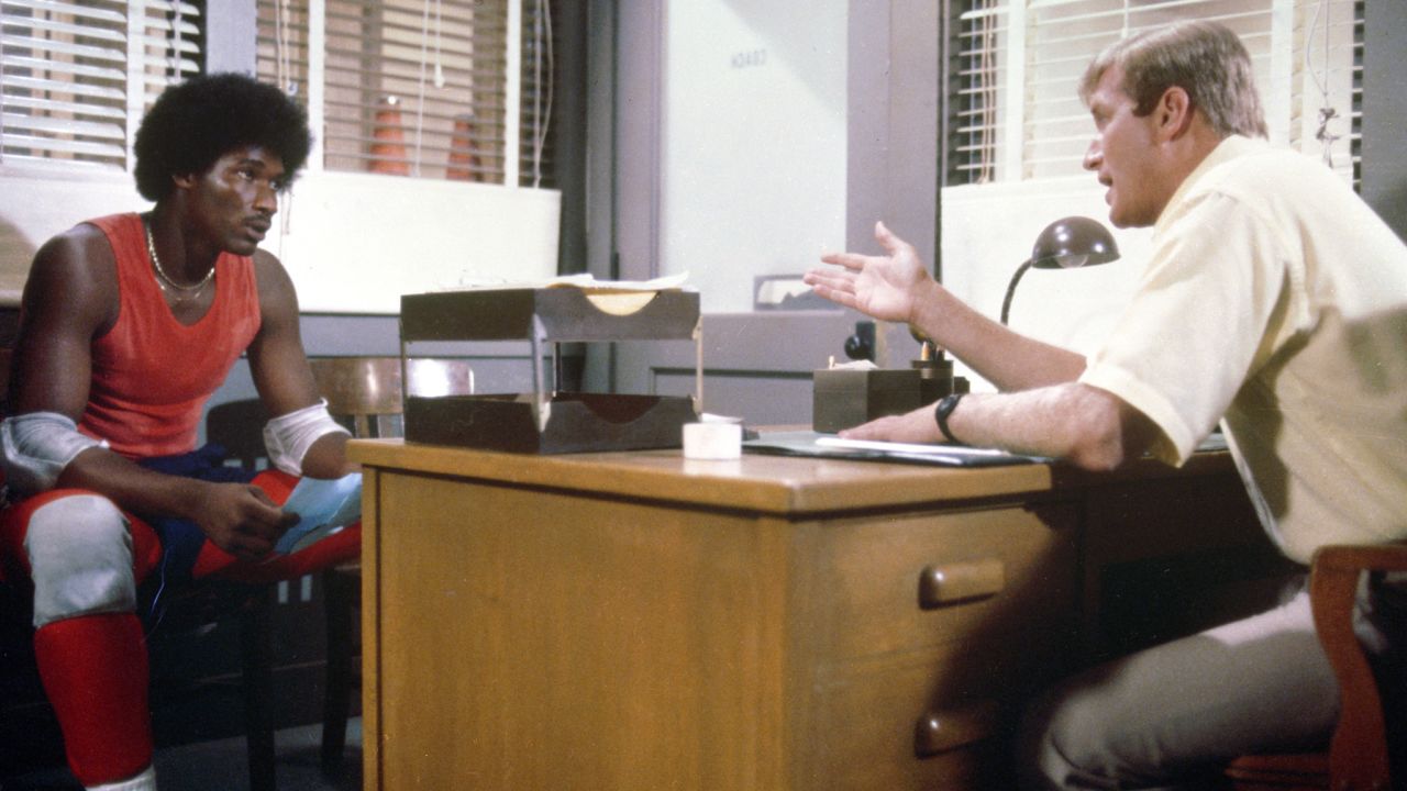 Still from the CBS dramatic television series 'The White Shadow' shows American actor Ken Howard (as high school basketball coach Ken Reeves) as he sits at his desk in his office and talks to actor Byron Stewart (as student and athlete Warren 'Cool' Coolidge), Los Angeles, 1979.