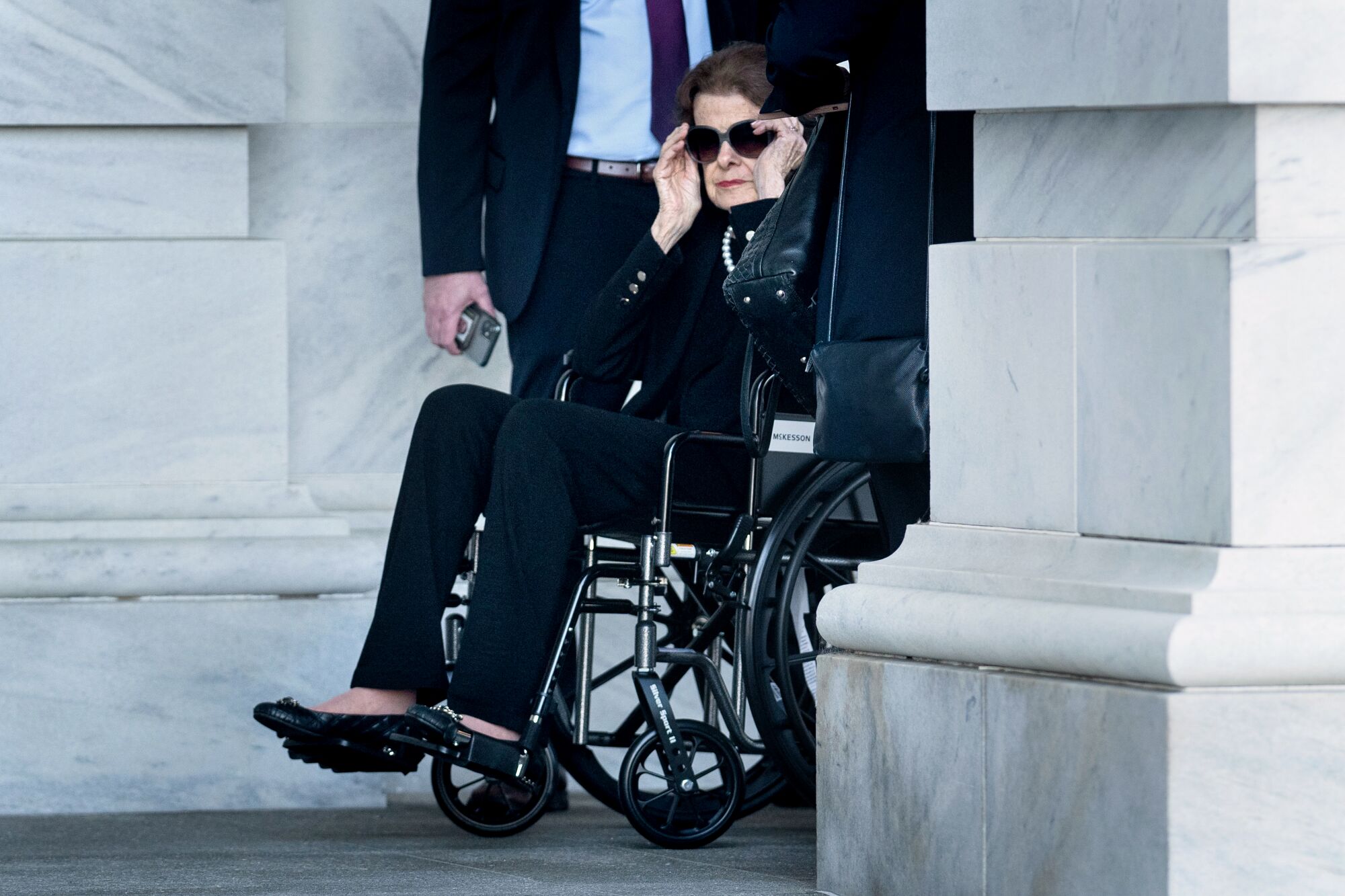 Sen. Dianne Feinstein adjusting her sunglasses as she exits the Capitol in a wheelchair.