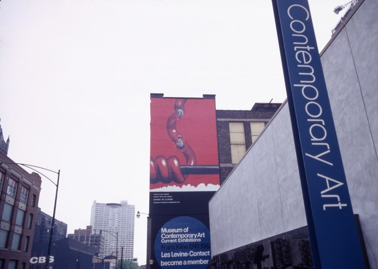 A billboard in the same location, outside the original MCA building, show a slick illustration of a red wire, wrapped around a black pole, the ends of which are coming unwrapped and are fraying.