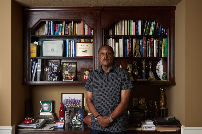 Tyrone stands in front of a bookshelf showcasing a few of his awards and family memorabilia at his home in Katy, Texas.