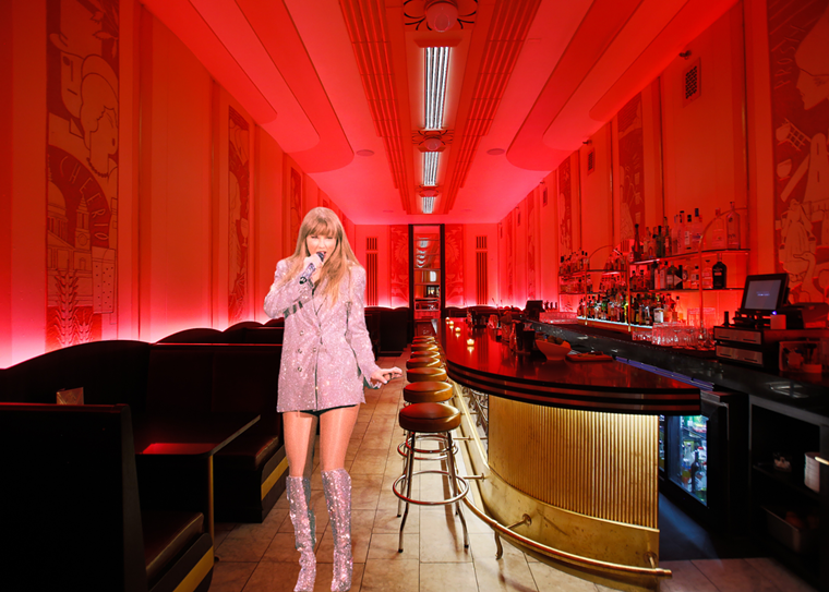 girl holding a micropone in a sparkly suit jacket in front of a bar with red lighting