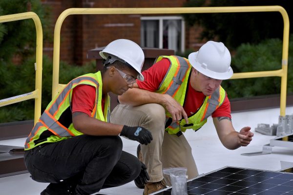 A woman and man work together to install solar panels in construction gear.