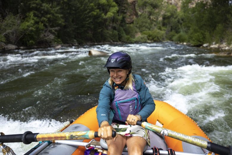 A woman row the oars on a raft in the middle of a whitewater river