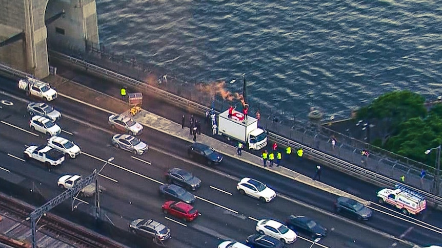 An aerial view looking down on Sydney Harbour Bridge, a truck with people on top letting off a flare can be seen.