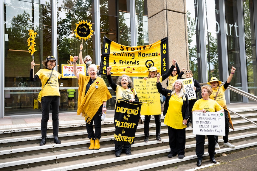 A group of women wearing bright yellow, hold signs like 'defend the right to protest' outside the NSW Supreme Court. 