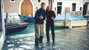 Alice Green Brown and Jonathan Sumrell wearing rain boot and standing in ankle-deep water in the calle by Casa Artom.