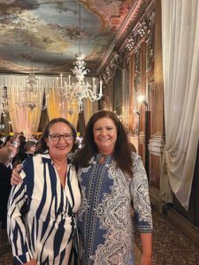 Two women at the gala. Behind them are chandeliers and ornate art