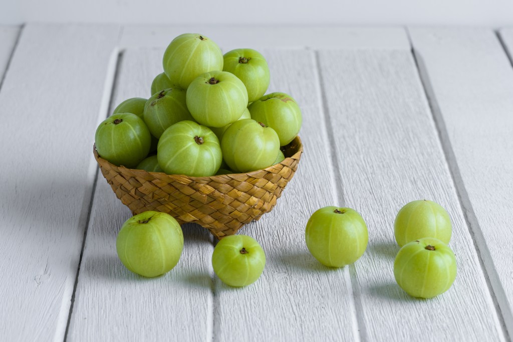 Indian gosseberries (aka amla) in a wicker bowl on a white wooden table