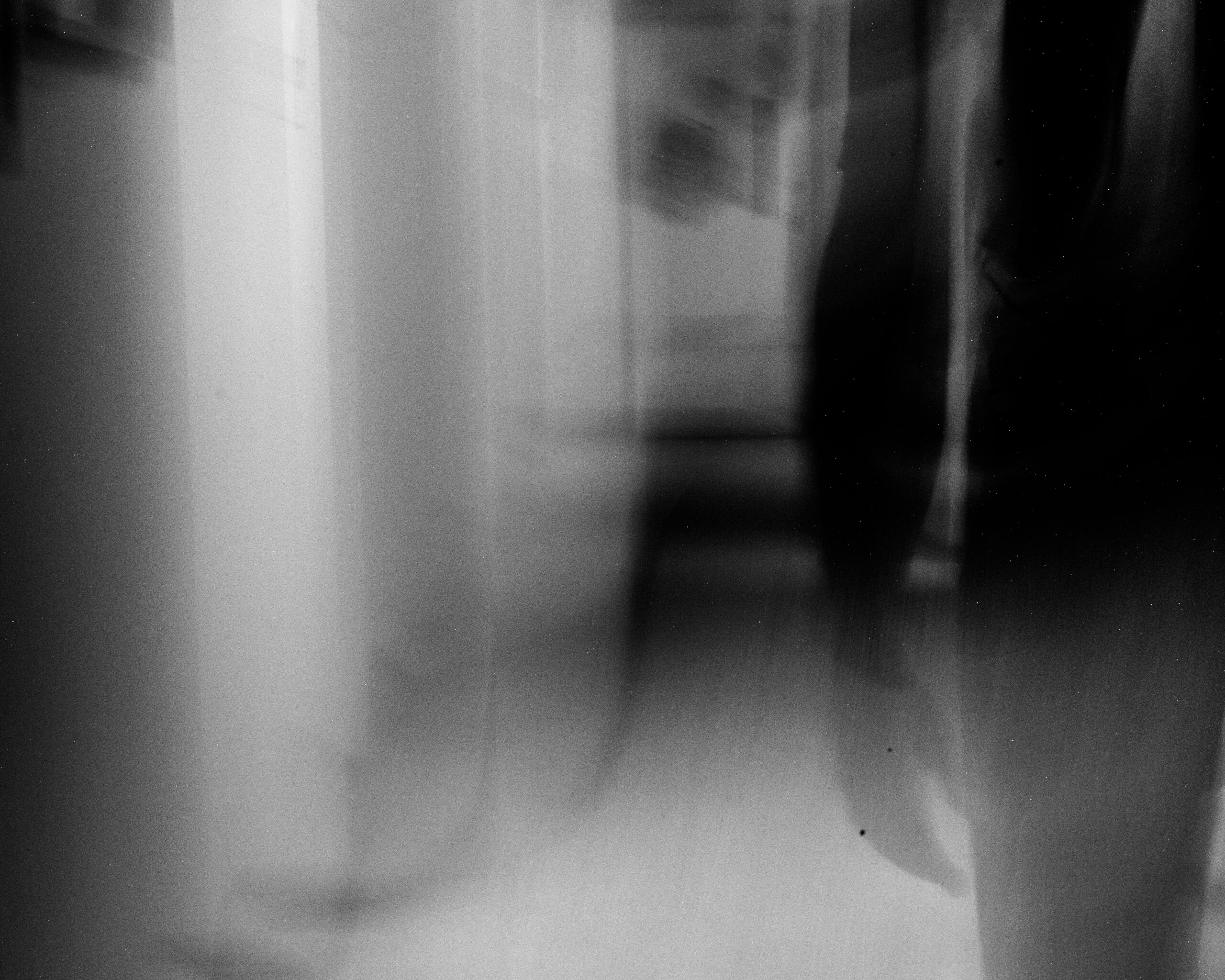 A silhouette of Rob Faubion seen walking through a hallway. The photo is stylishly blurred and black and white, giving it a ghostly feeling.