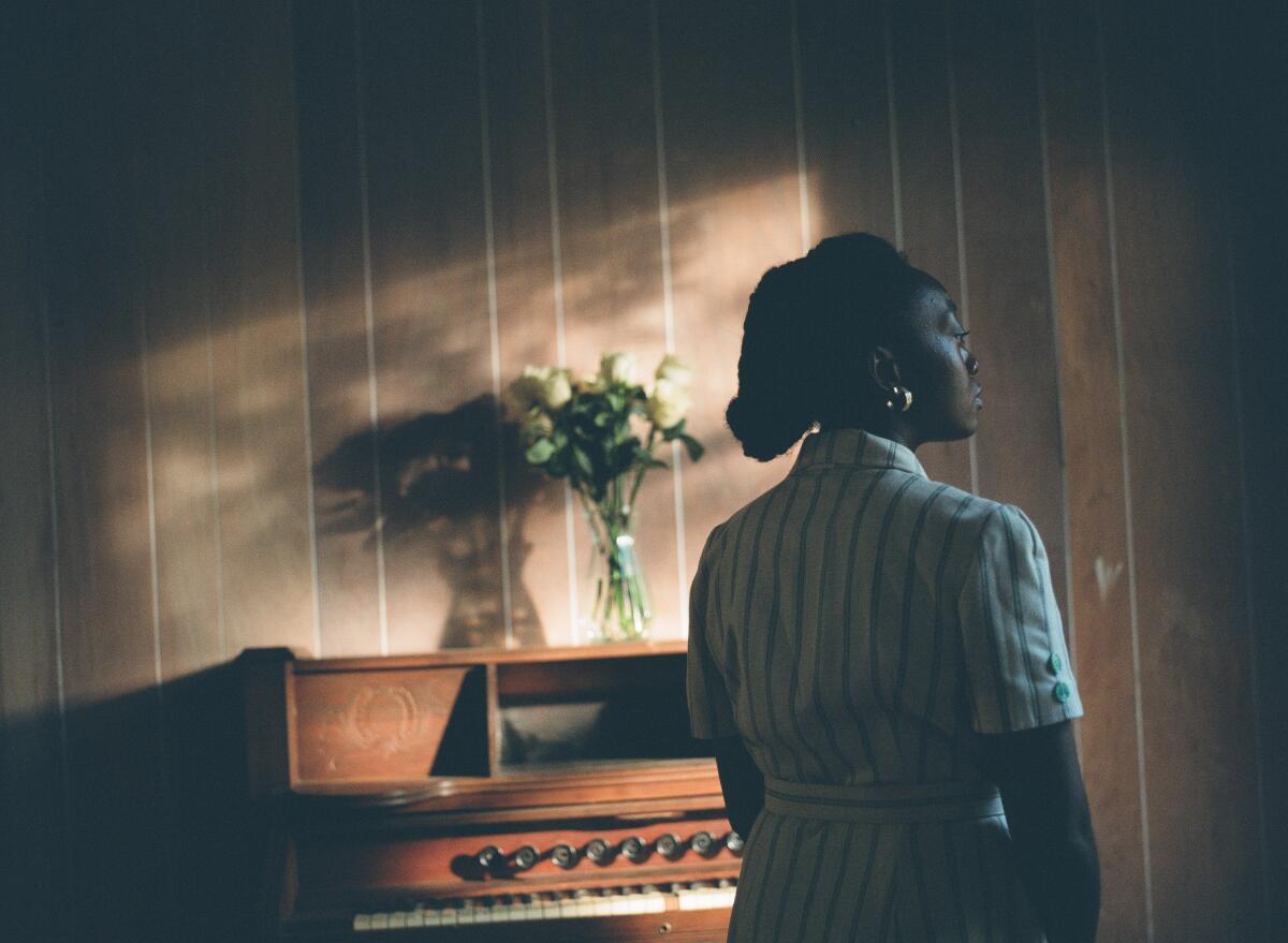 A teenage girl stands beside a piano.