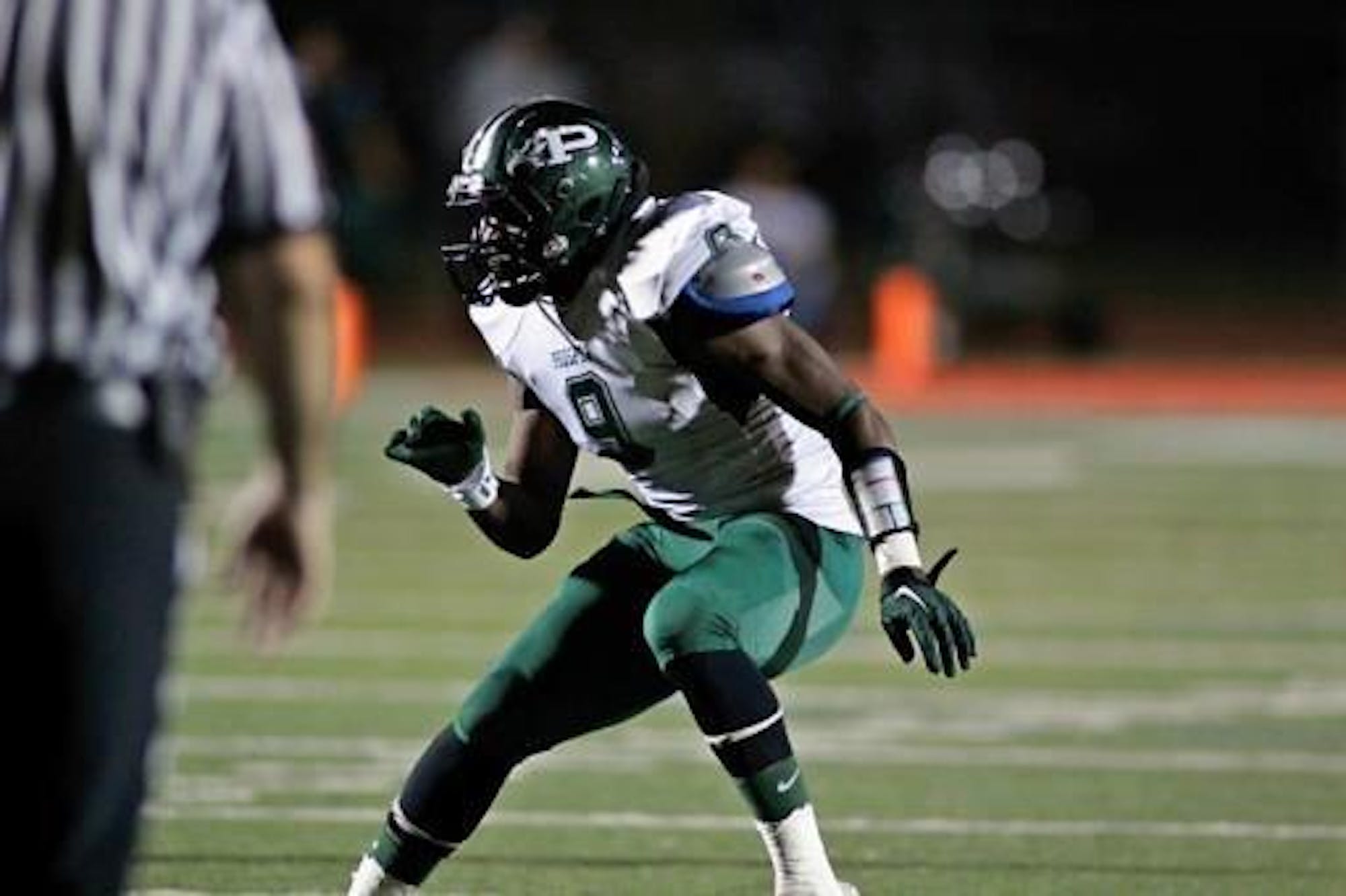 Black male wearing a white and green football uniform backpedals during a football game.