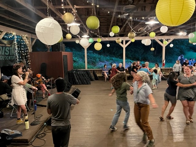 People square dance in a ballroom. Balloons are shown on the ceiling.