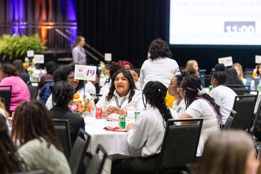 Young women gather around tables for roundtable discussions.
