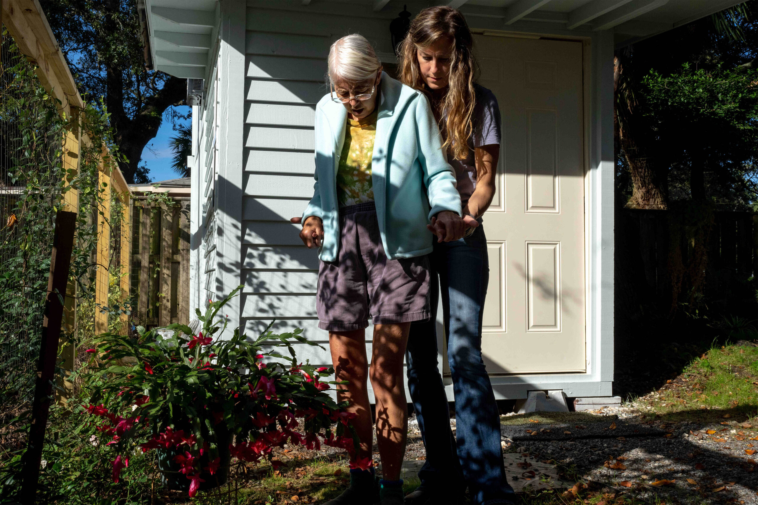 A photo of a caretaker helping an elderly woman walk outside.