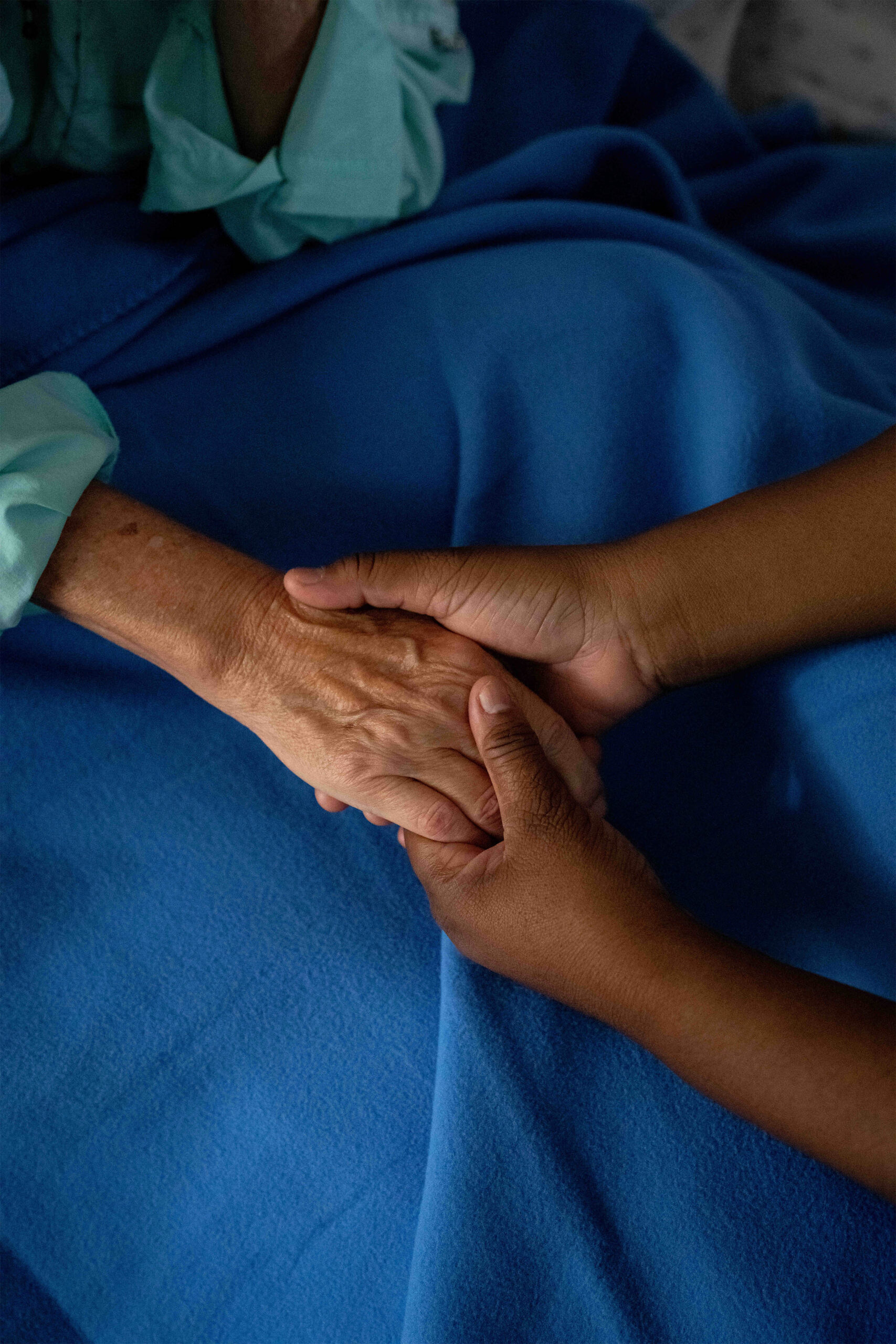 A photo of a caregiver holding an elderly woman's hand.