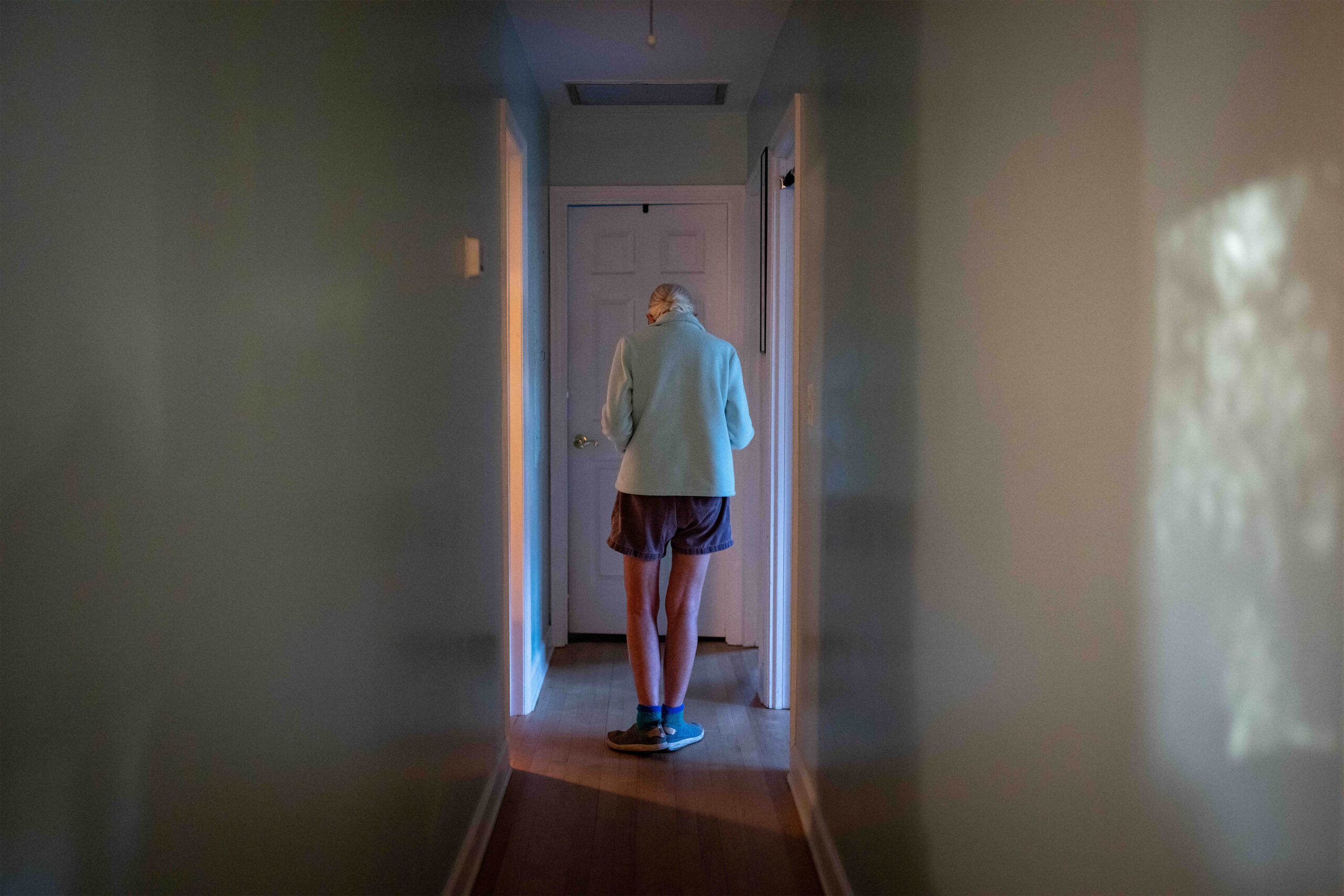 A photo of an elderly woman walking down a hallway indoors.