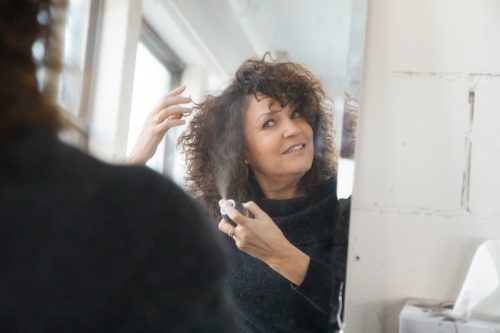 Mature woman applying hair spray to her lustrous mane in front of mirror.