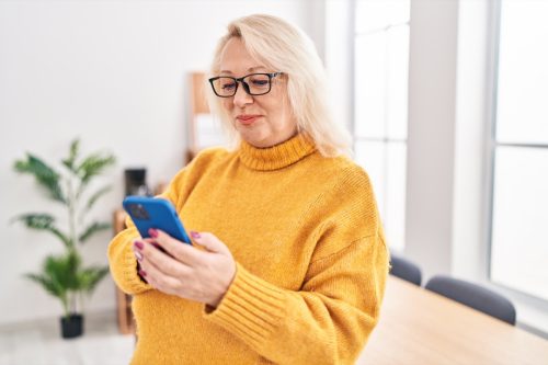 Middle age blonde woman business worker using smartphone at office