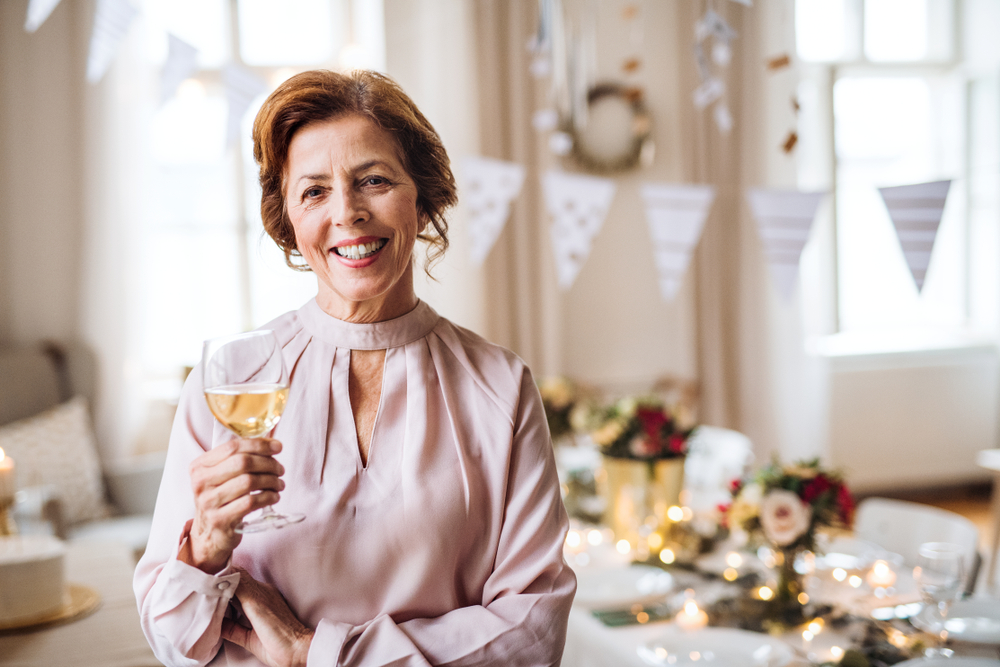 Portrait of smiling senior woman in pink blouse hosting a party with wine or champagne