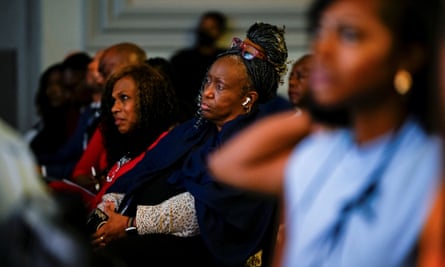 Looking through blurry foreground at two older Black women with long curly hair listening intently.