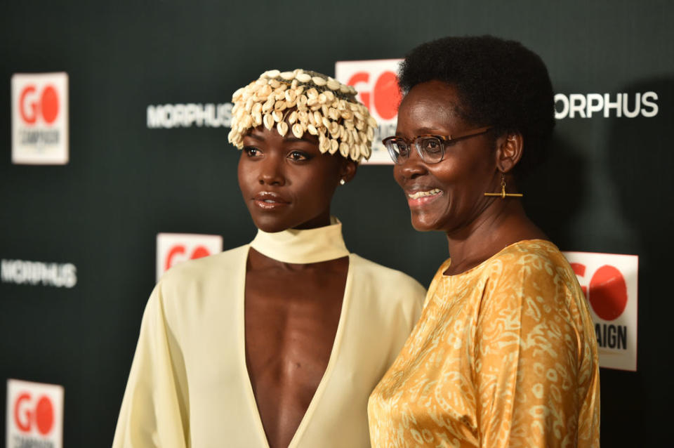 Lupita Nyong'o in a deep v-neck dress decorated with shells and accompanied by Dorothy Nyong'o in a golden dress at a GO Campaign event